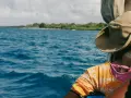 Persona con cappello di paglia osserva il mare blu e la costa verde. Un viaggio in Kenya è un'ottima idea per godersi questo panorama.