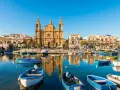 Barche colorate nel porto di Marsaxlokk, Malta. Un luogo incantevole dove dormire a Malta, con la chiesa barocca che domina lo sfondo.