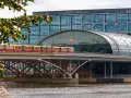 Treno giallo e rosso attraversa un ponte sopra un fiume, con la moderna stazione ferroviaria di Berlino sullo sfondo. Un ottimo modo per capire come muoversi a Berlino.