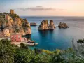 Un borgo con torri antiche e un edificio rosso si affaccia su un mare cristallino, perfetto per le mete estive in Italia.