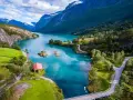 Un lago turchese serpeggia tra montagne verdi e innevate. Un piccolo edificio rosso si affaccia sull'acqua. La crociera fiordi periodo migliore è l'estate per godere di questi panorami.