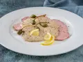 Vitello tonnato, uno dei piatti tipici torinesi, con salsa cremosa, capperi e limone su un piatto bianco.