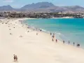 Spiaggia affollata con persone che passeggiano e si rilassano, hotel e montagne sullo sfondo. Questo è il paesaggio di Fuerteventura, dove si trova questo paradiso.