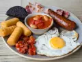 Un abbondante piatto per scoprire cosa mangiare a Londra: uova, salsiccia, fagioli, pomodorini, pane nero e crocchette.
