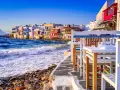 Case vacanza a Mykonos, un'idea per dove andare a vivere all'estero con pochi soldi. Case bianche sul mare, onde che si infrangono sugli scogli, tavoli di un ristorante.
