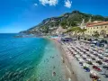 Spiaggia affollata con ombrelloni e gente che nuota, un'ottima idea per un weekend in Italia con vista sulla costa.