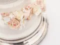 Dettaglio di una torta nuziale a più piani, decorata con pizzo e fiori di zucchero rosa e bianchi, su un elegante vassoio argentato.