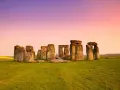 Stonehenge, un misterioso cerchio di pietre antiche, si erge su un prato verde sotto un cielo rosa e viola. Un'icona di Londra e della storia.