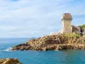Torre medievale e mare blu a Calafuria, con scogli rocciosi e cielo nuvoloso.