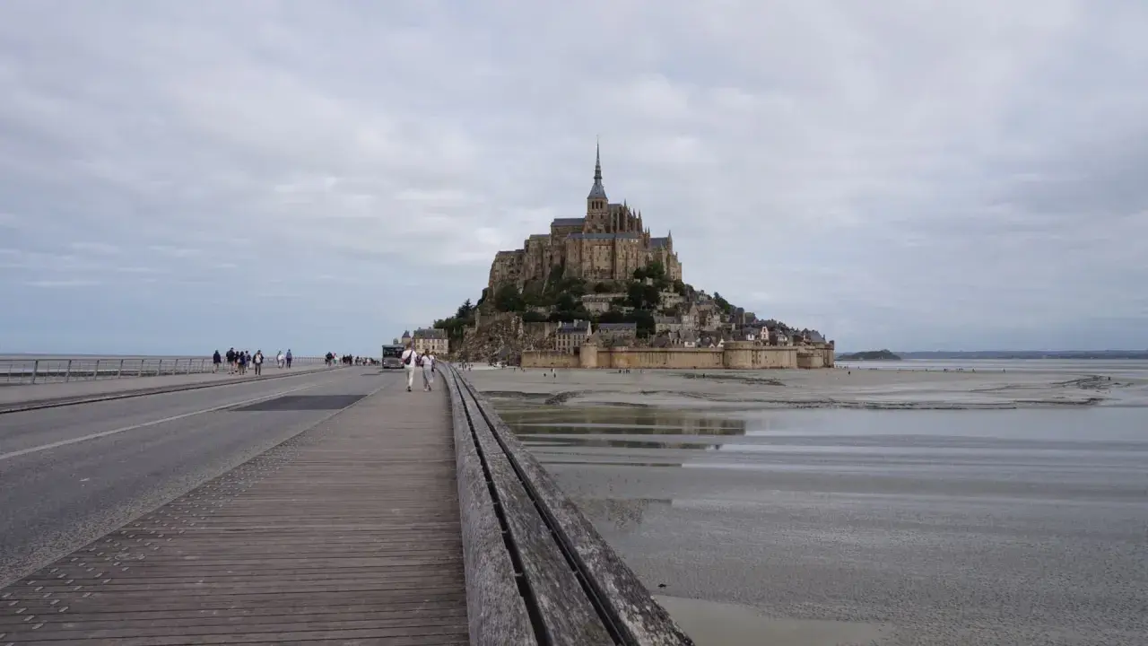 Un'imponente abbazia domina l'isola di Mont Saint-Michel, collegata alla terraferma da un ponte pedonale e una strada.