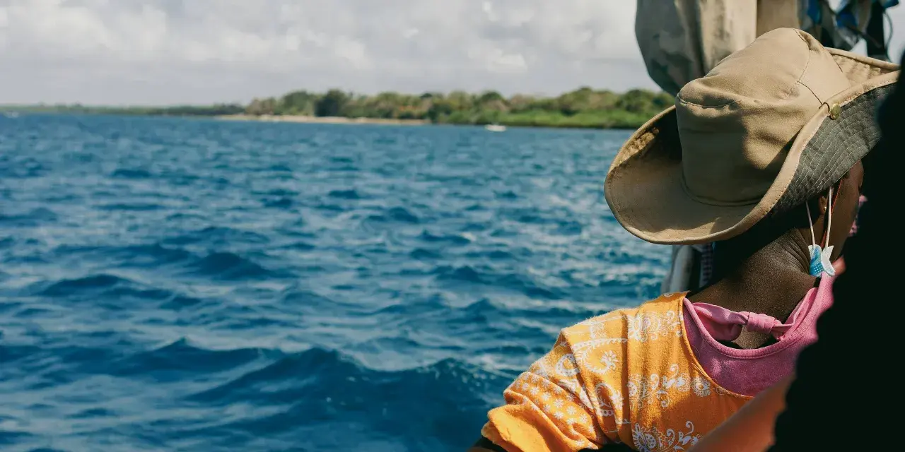 Persona con cappello di paglia osserva il mare blu e la costa verde. Un viaggio in Kenya è un'ottima idea per godersi questo panorama.
