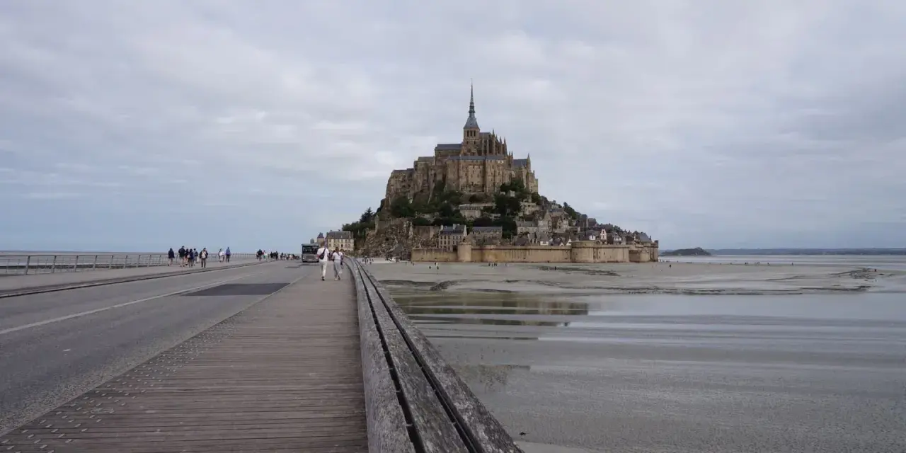 Un'imponente abbazia domina l'isola di Mont Saint-Michel, collegata alla terraferma da un ponte pedonale e una strada.