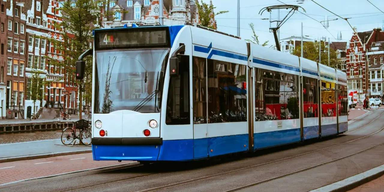 Un tram bianco e blu sferraglia sui binari, un modo efficiente per capire come muoversi ad Amsterdam tra case storiche e canali.