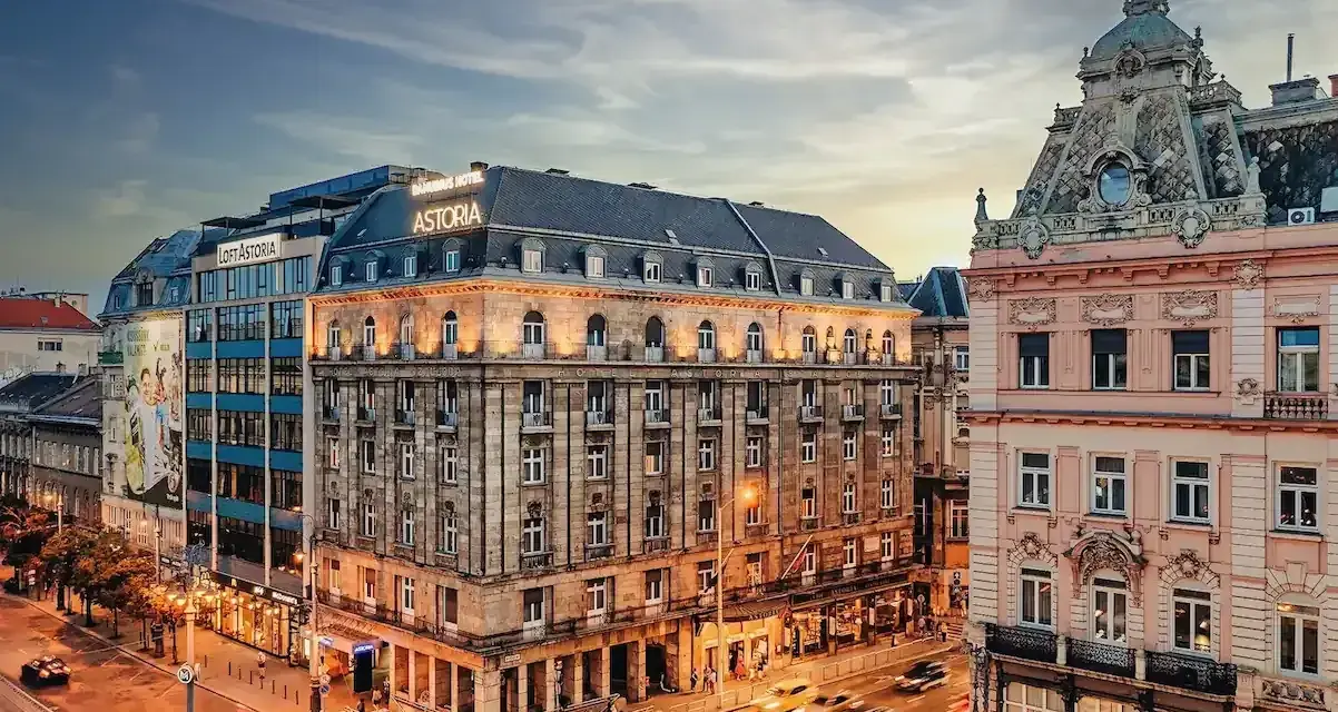 Hotel Astoria, un'ottima scelta per dove alloggiare a Budapest, si affaccia su una strada trafficata con auto gialle sfocate.