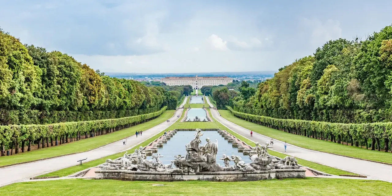 Giardini maestosi con fontane barocche e un palazzo imponente in lontananza, ricordano i fasti dei mulini reali.