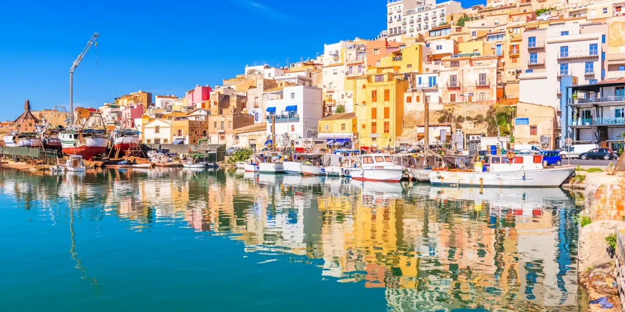 Porto di Sciacca, cosa vedere: barche da pesca ormeggiate e case colorate che si specchiano sull'acqua cristallina.
