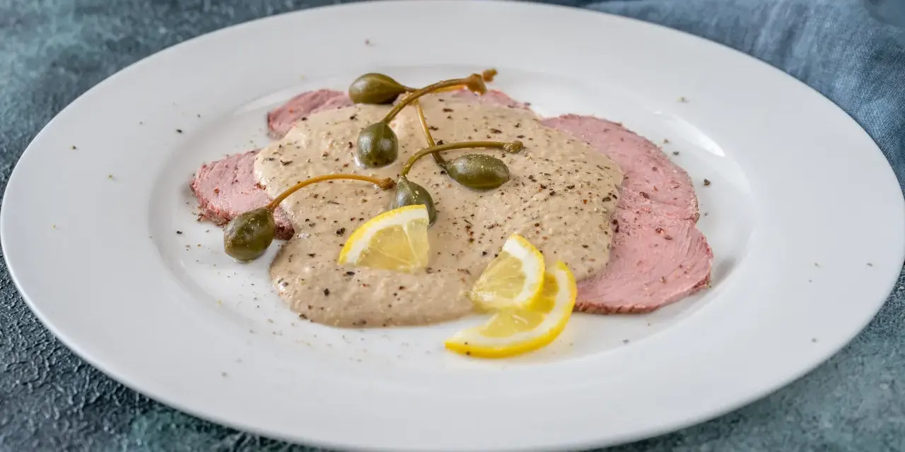 Vitello tonnato, uno dei piatti tipici torinesi, con salsa cremosa, capperi e limone su un piatto bianco.