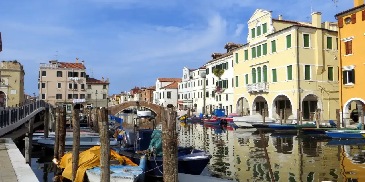 Chioggia cosa vedere: un canale con barche ormeggiate e case colorate che si riflettono sull'acqua.