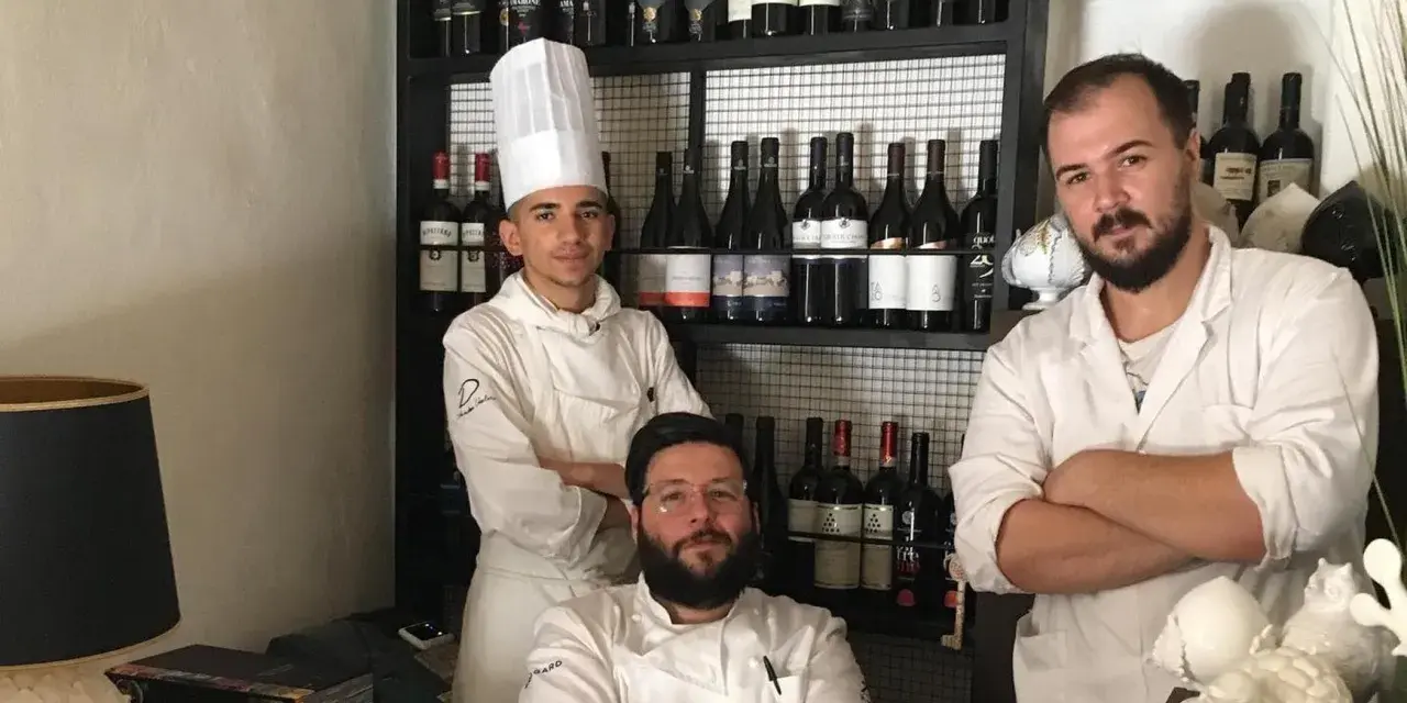 Tre chef posano davanti a una cantina di vini in un ristorante stellato Puglia.