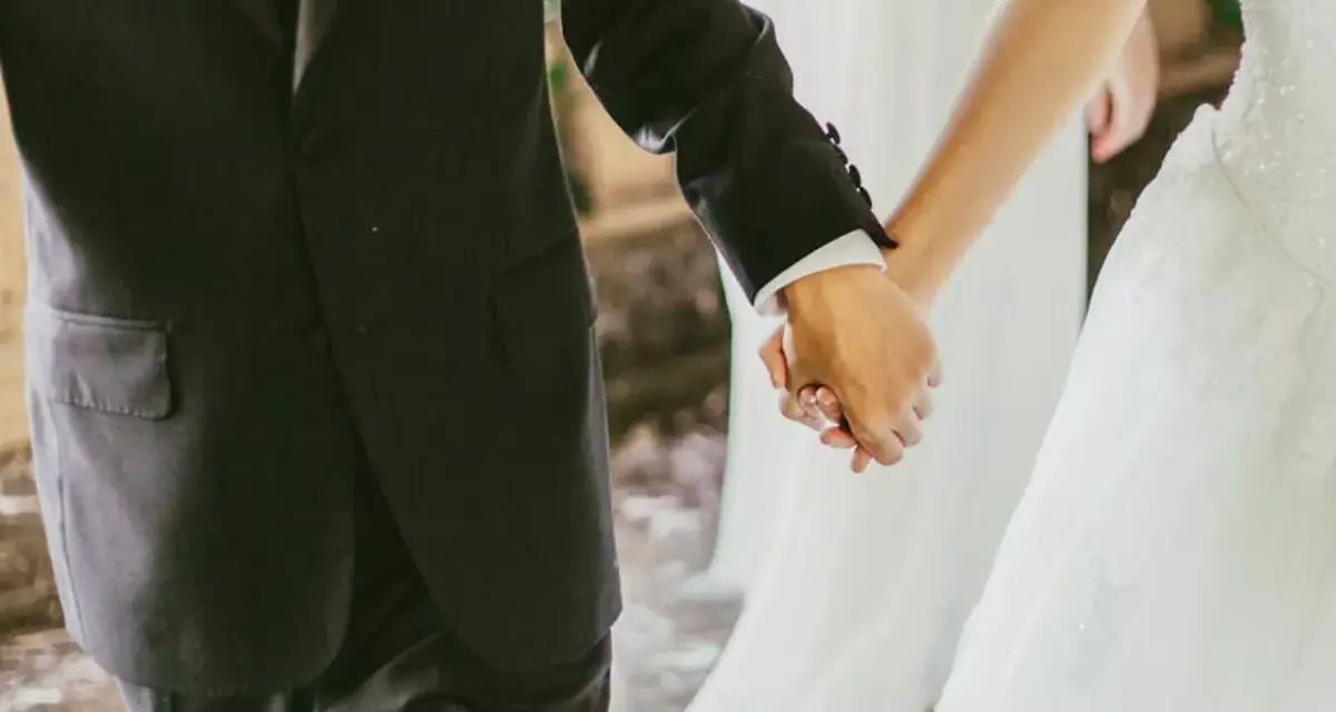 Mani intrecciate, un uomo in abito scuro e una sposa in bianco. Il vero significato di sposa è l'amore che unisce.