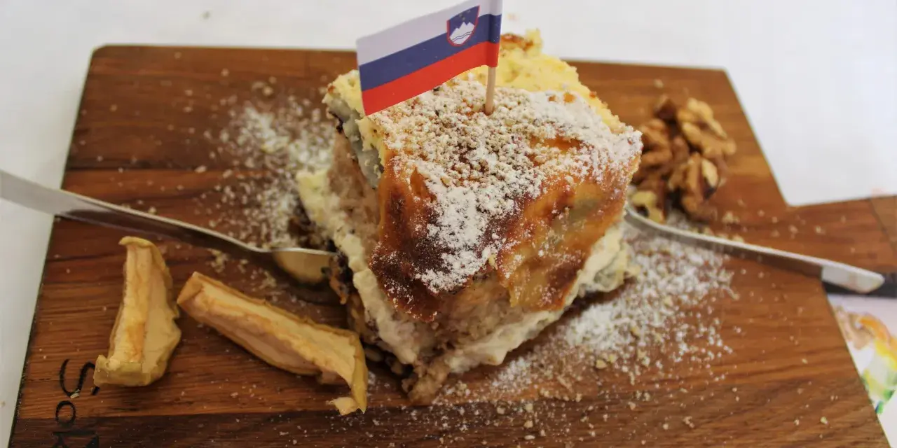 Una fetta di torta con bandierina slovena, noci e mele essiccate, un assaggio dei piatti tipici sloveni.