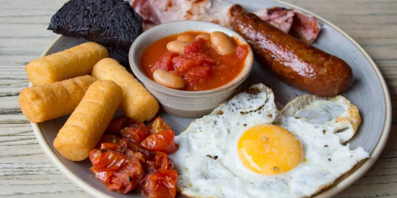Un abbondante piatto per scoprire cosa mangiare a Londra: uova, salsiccia, fagioli, pomodorini, pane nero e crocchette.