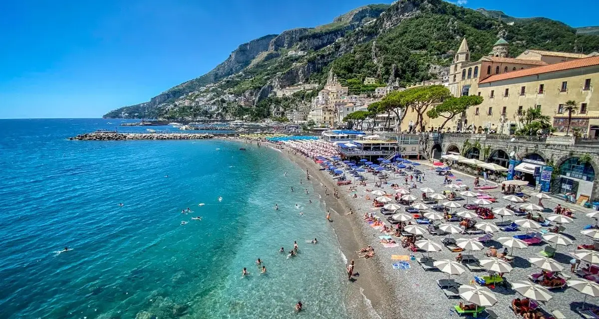 Spiaggia affollata con ombrelloni e gente che nuota, un'ottima idea per un weekend in Italia con vista sulla costa.