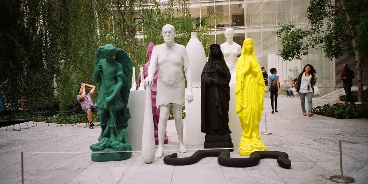 Sculture colorate e una figura in nero nel moma garden. Un serpente nero si snoda tra le statue.