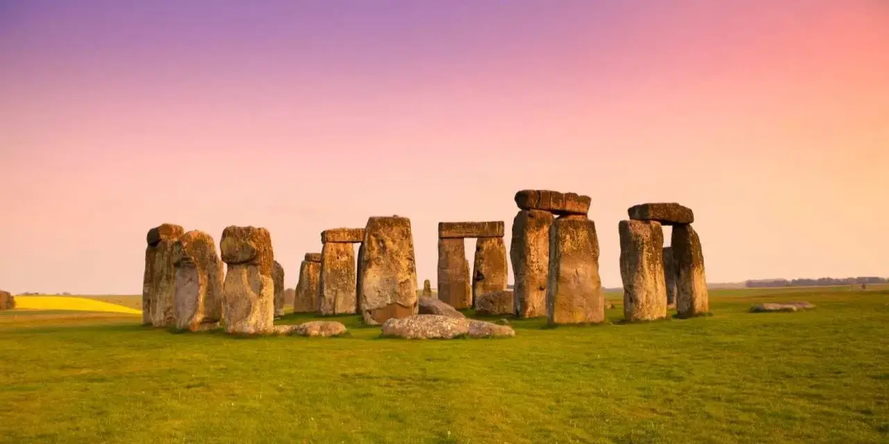 Stonehenge, un misterioso cerchio di pietre antiche, si erge su un prato verde sotto un cielo rosa e viola. Un'icona di Londra e della storia.