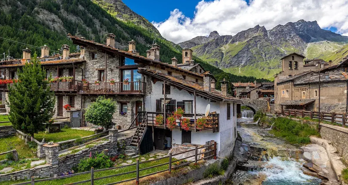 Un incantevole borgo da visitare in Piemonte, con case in pietra, balconi fioriti e un torrente che scorre tra le montagne.