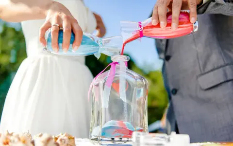 Sposi uniscono sabbia blu e rossa in un vaso, un simbolo del rito della sabbia che unisce le loro vite.