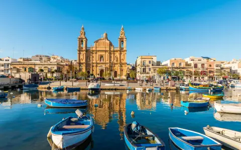 Barche colorate nel porto di Marsaxlokk, Malta. Un luogo incantevole dove dormire a Malta, con la chiesa barocca che domina lo sfondo.