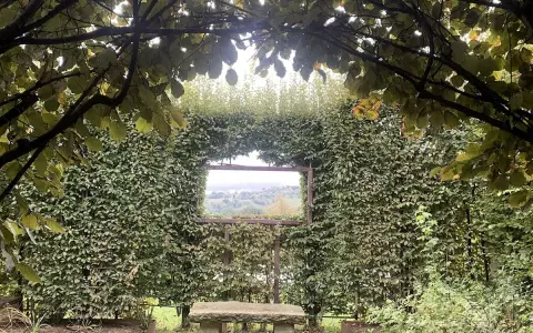 Un angolo verde incantevole, con un sedile in pietra che invita alla contemplazione del paesaggio visibile attraverso un'apertura nella siepe, come una finestra sul **palazzo di Cuzzano**.