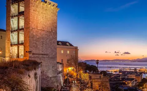 Torre medievale illuminata al tramonto, con vista sul porto e sul mare. Un'ottima anteprima di cosa vedere a Cagliari in un giorno.
