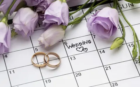 Anelli d'oro su un calendario segnato con "Wedding" e fiori lilla. Il giorno perfetto quando sposarsi.