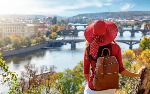Donna con cappello rosso ammira Praga in autunno. Il periodo migliore per andare a Praga è quando la natura si tinge di colori caldi.