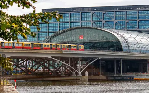 Treno giallo e rosso attraversa un ponte sopra un fiume, con la moderna stazione ferroviaria di Berlino sullo sfondo. Un ottimo modo per capire come muoversi a Berlino.