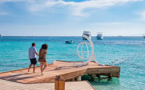Coppia passeggia su un molo di legno a **Orgada Egitto**, con acque turchesi e barche all'orizzonte.