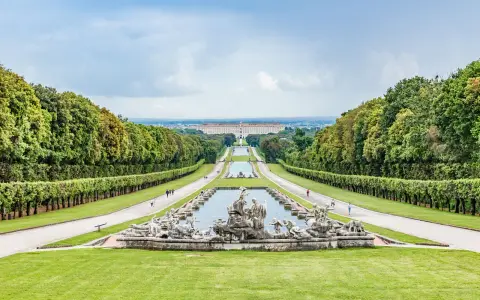 Giardini maestosi con fontane barocche e un palazzo imponente in lontananza, ricordano i fasti dei mulini reali.