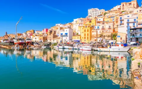 Porto di Sciacca, cosa vedere: barche da pesca ormeggiate e case colorate che si specchiano sull'acqua cristallina.