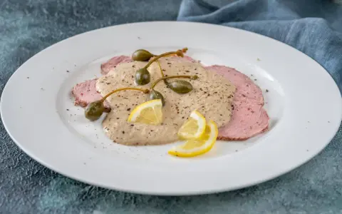 Vitello tonnato, uno dei piatti tipici torinesi, con salsa cremosa, capperi e limone su un piatto bianco.