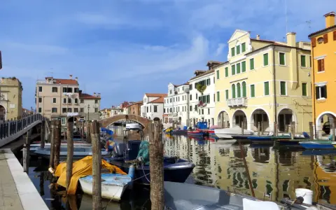 Chioggia cosa vedere: un canale con barche ormeggiate e case colorate che si riflettono sull'acqua.