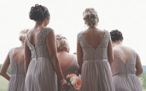 Cinque donne con abiti da damigella, una tiene un bouquet. Si percepisce la differenza tra damigella e testimone.