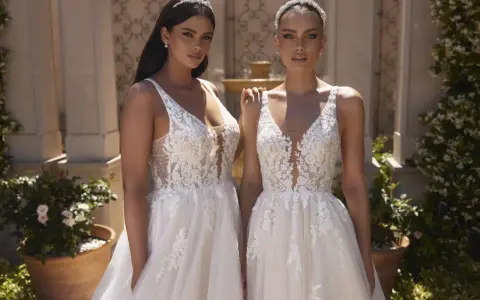 Due modelle con abiti da sposa in pizzo, con diversi tipi di scollatura a V e dettagli floreali, posano all'aperto.