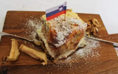 Una fetta di torta con bandierina slovena, noci e mele essiccate, un assaggio dei piatti tipici sloveni.
