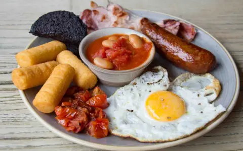 Un abbondante piatto per scoprire cosa mangiare a Londra: uova, salsiccia, fagioli, pomodorini, pane nero e crocchette.