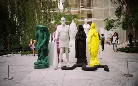 Sculture colorate e una figura in nero nel moma garden. Un serpente nero si snoda tra le statue.
