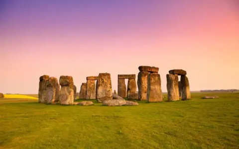 Stonehenge, un misterioso cerchio di pietre antiche, si erge su un prato verde sotto un cielo rosa e viola. Un'icona di Londra e della storia.