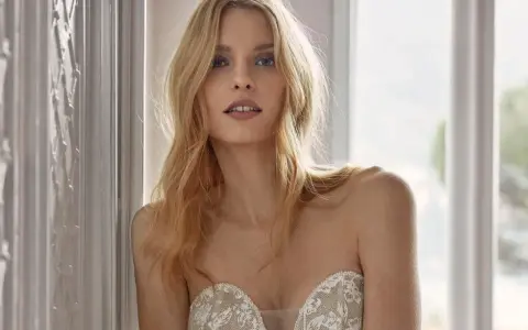 Modella con un trucco da sposa semplice, capelli biondi sciolti e un abito in pizzo.