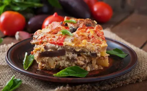 Un assaggio di cosa mangiare a Santorini: una saporita moussaka con melanzane, pomodori e formaggio, guarnita con basilico fresco.